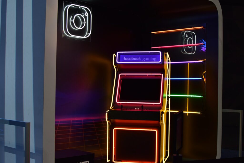 A neon arcade cabinet with the logo for Facebook Gaming is in a neon room, in this article you can learn how to stream games to Facebook.