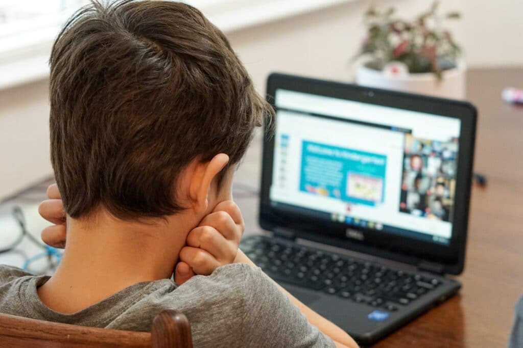 A child photographed from behind looking at their online class.