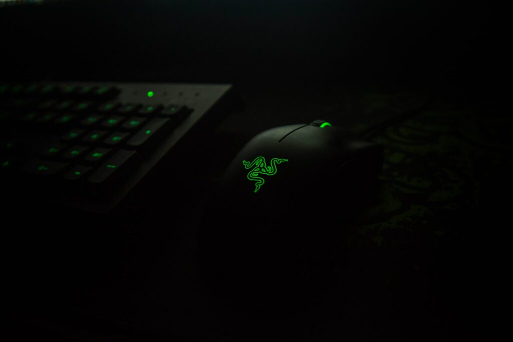 An affordable Razer mouse on a desk next to a keyboard with their green RGB lights on.