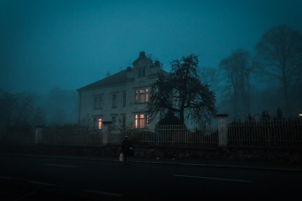 A person stood in front of a spooky house at night.