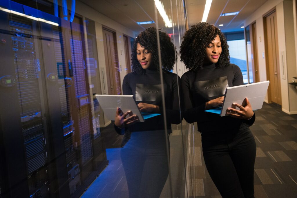 A person stands next to a server room, holding their laptop, giving a presentation from anywhere with media can lead to better online meetings.