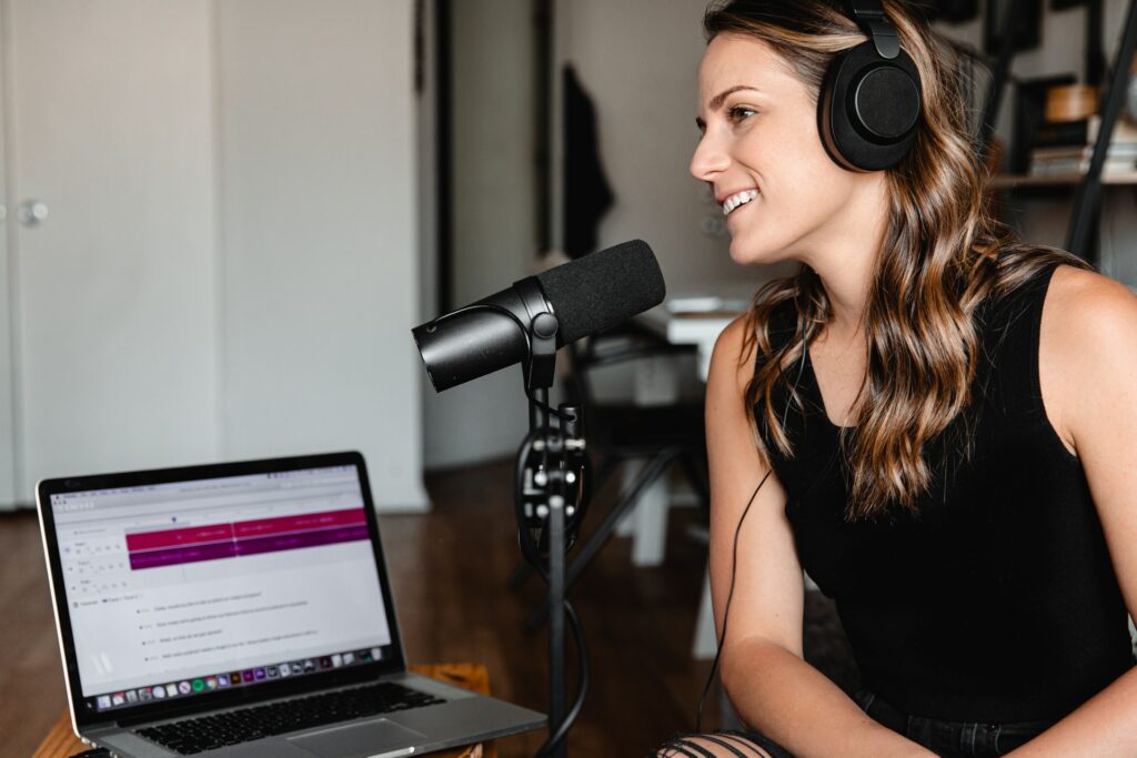 A person sat in front of a microphone talking in to a large microphone which is on a stand connected to a PC taking part in virtual talk shows.