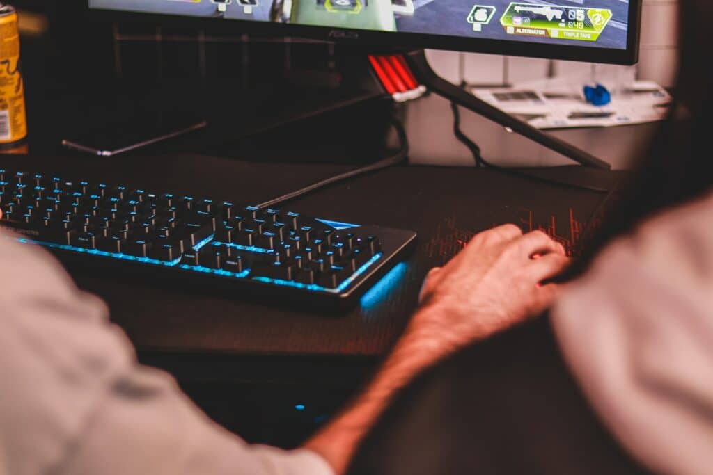 An image of a hand on a mouse in front of a gaming PC with a keyboard on a desk, no doubt looking for Free Streaming Tools!