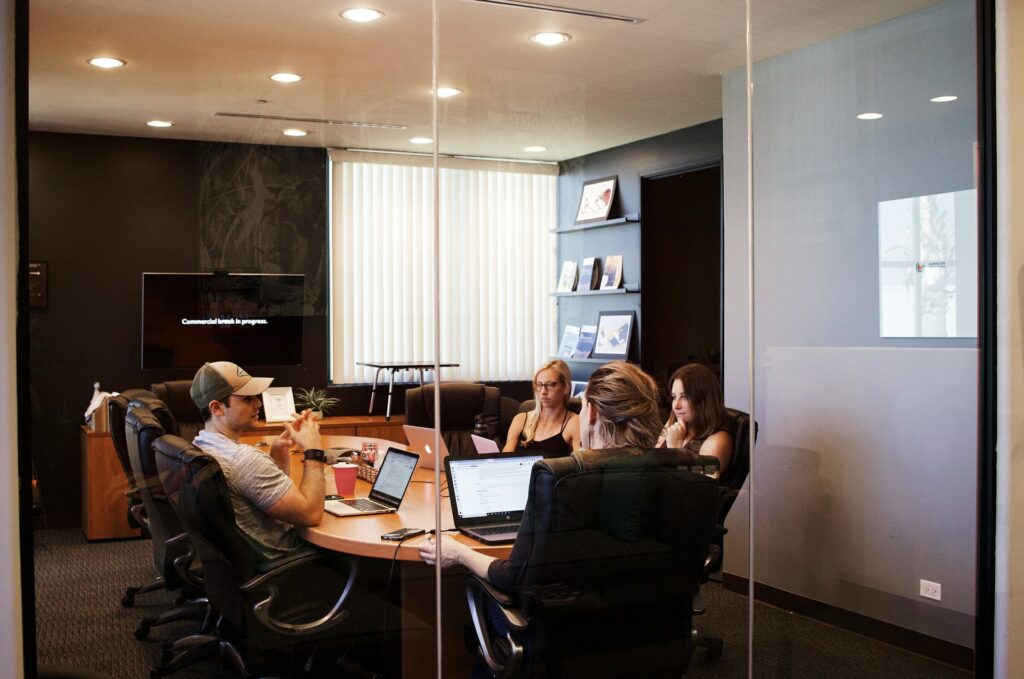 Four people sat in a conference room with a large screen at the end of it to help with a hybrid office balance.
