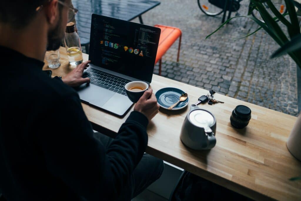 A person sat in a cafe having a coffee whiule working at the same time, multitaking can contribute to zoom fatigue.
