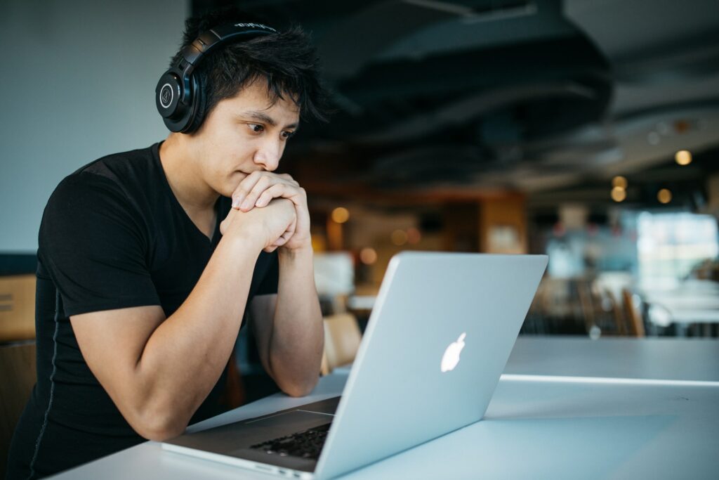 A person sat at a desk with headphones on in a cafe watching a video on a laptop the person who made the video knew how to make an online course.