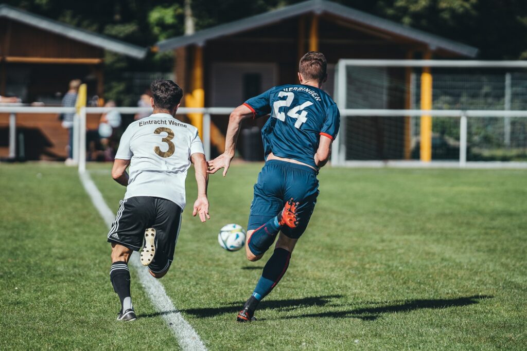 Two people playing football on a green field in sunlight running for the ball which you could watch online if you learn how to livestream your local sports event.