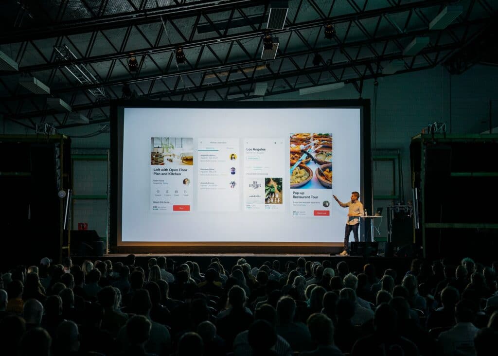 A person stood in front of a large screen giving a presentation knowing how to make a pitch deck.
