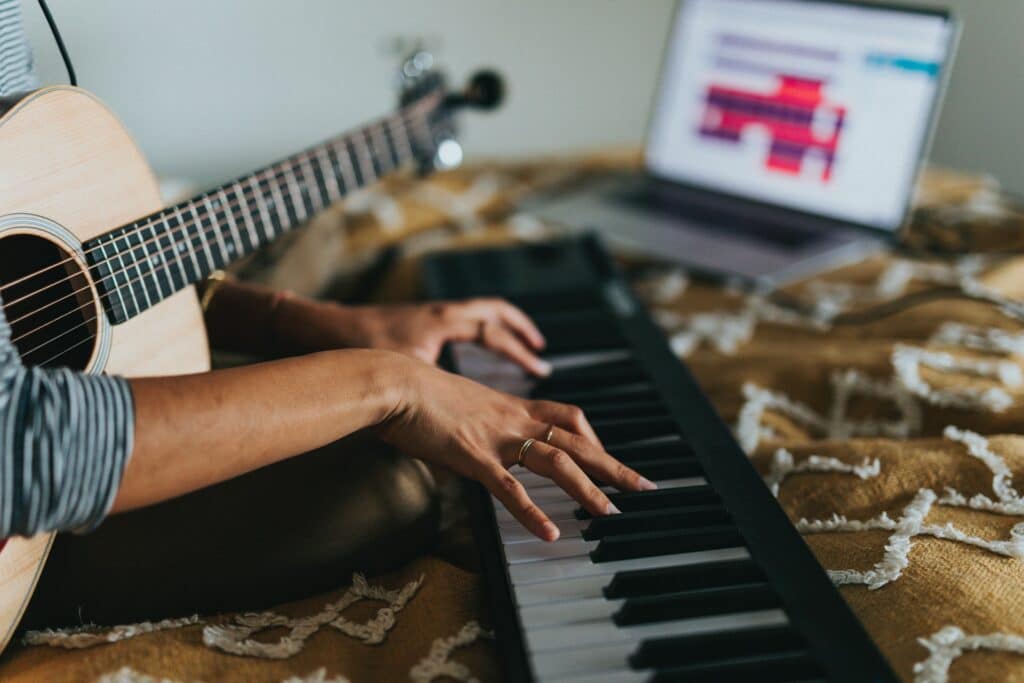 A person plays a keyboard connected to a laptop as they live stream music