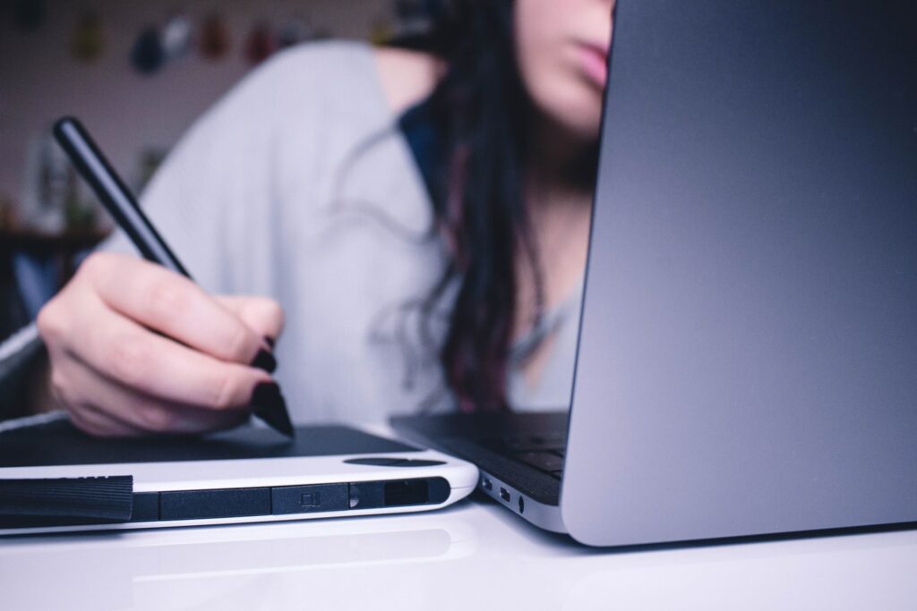 A person draws on a wacom tablet connected to their laptop which could also stream digital art.