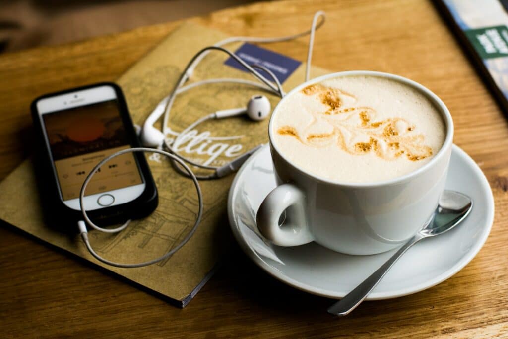 A latte sits on a table next to an iPhone which is listening to a livestreamed podcast.
