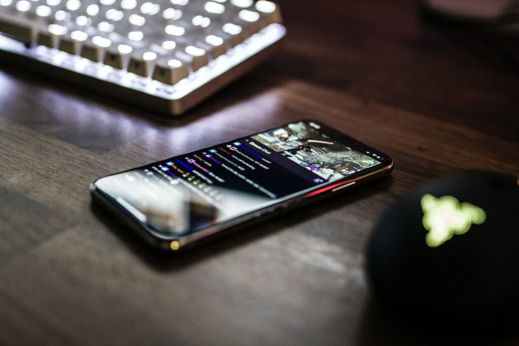 A close up of a phone next to a gaming mouse and keyboard on a desk watching a live stream, adding live streaming automation could help you!