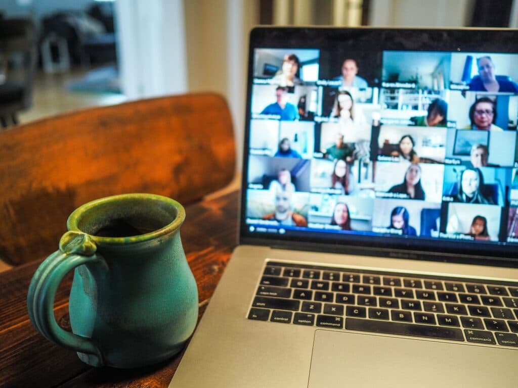 A laptop on a desk with a large virtual all-hands meeting displayed on it with a mug sat next to the laptop.