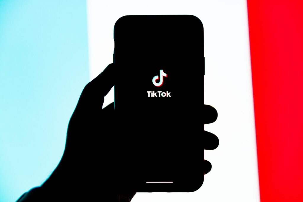 A phone showing the TikTok logo on a bright background being held by a hand in shadow showing streamers using TikTok
