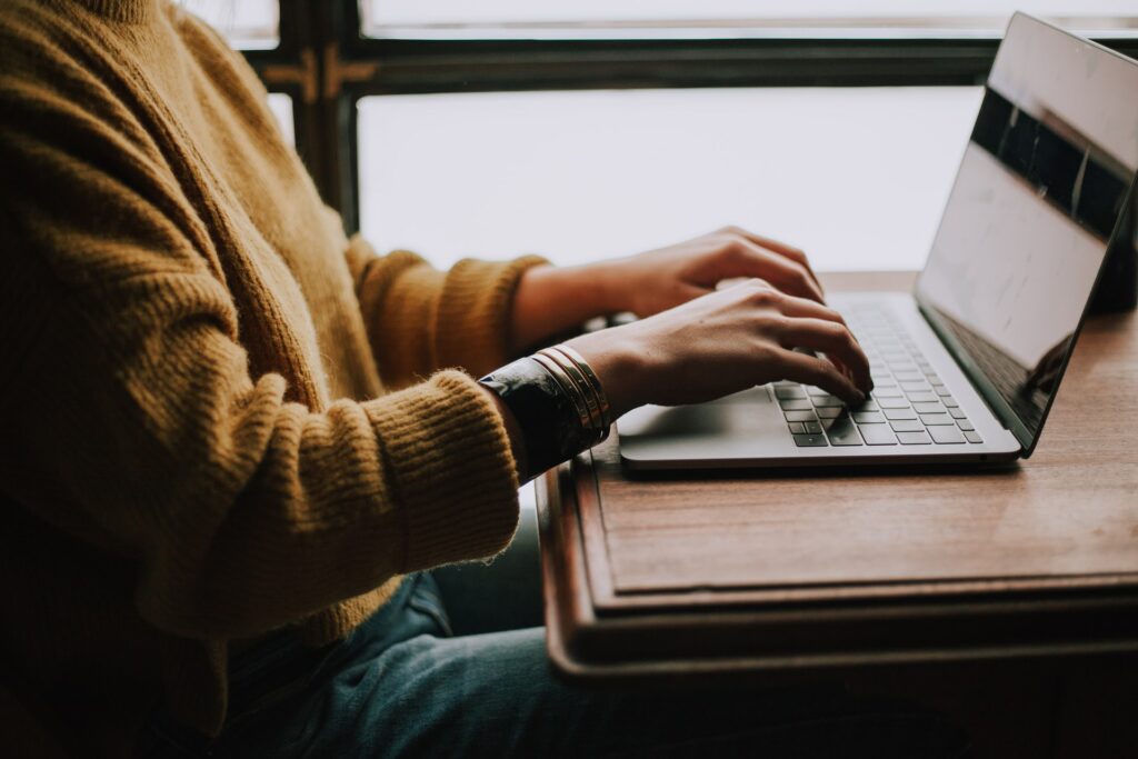 Someone sat, side on, using their laptop on their kitchen table, working from home requires some remote team motivation.