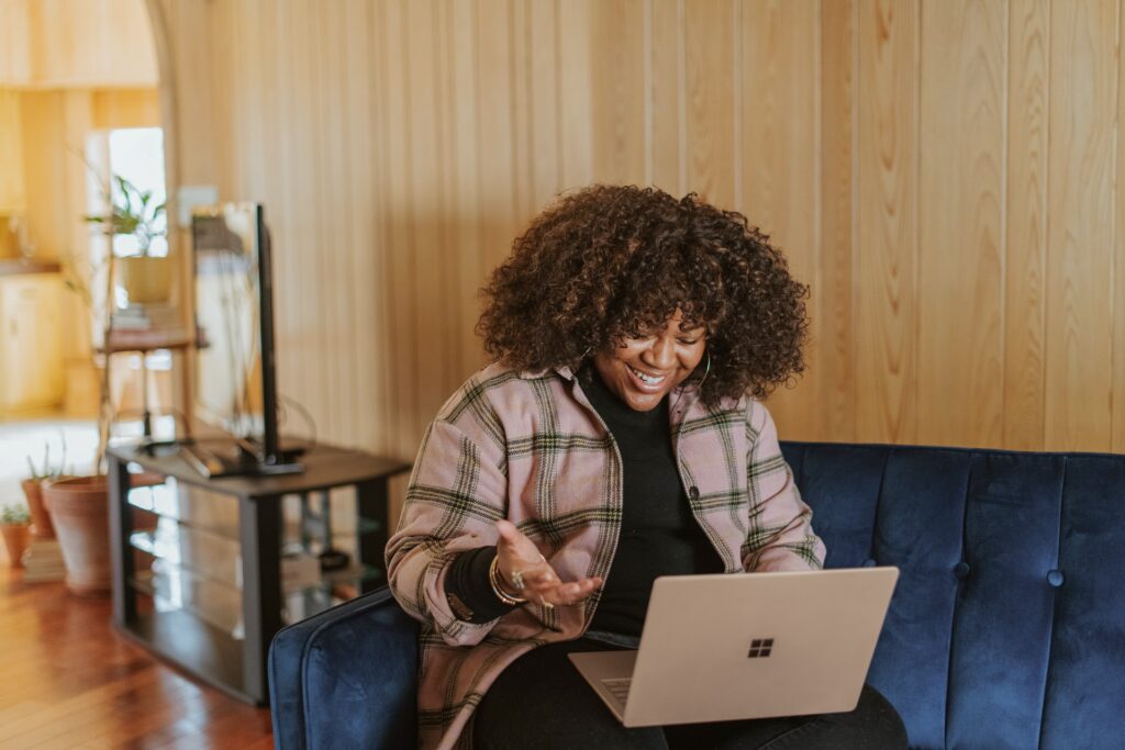 A person sits on a sofa, talking on their laptop to a colleague from home, remote team motivation is important to keep everyone happy and productive!