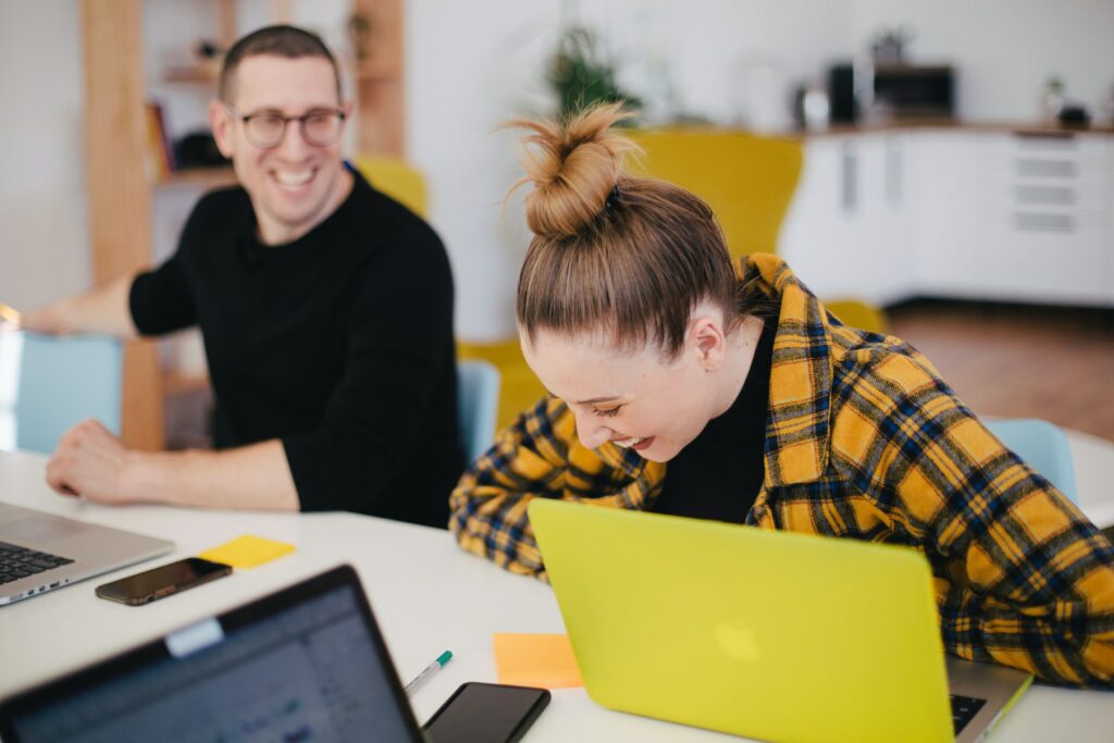 Two people, both laughing, one looking at a laptop at better email, a video sent rather than a wall of text!