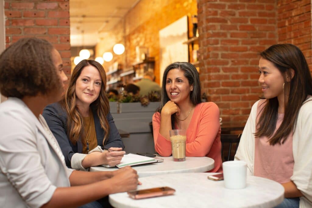 Four people sat around a table, one taking notes, the others have coffee and a phone is in front of the person speaking, listening is key to improve workplace communications