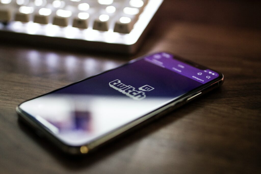 A smartphone is on a desk with a keyboard behind it displaying the Twitch app, a place you could stream to with multistreaming.