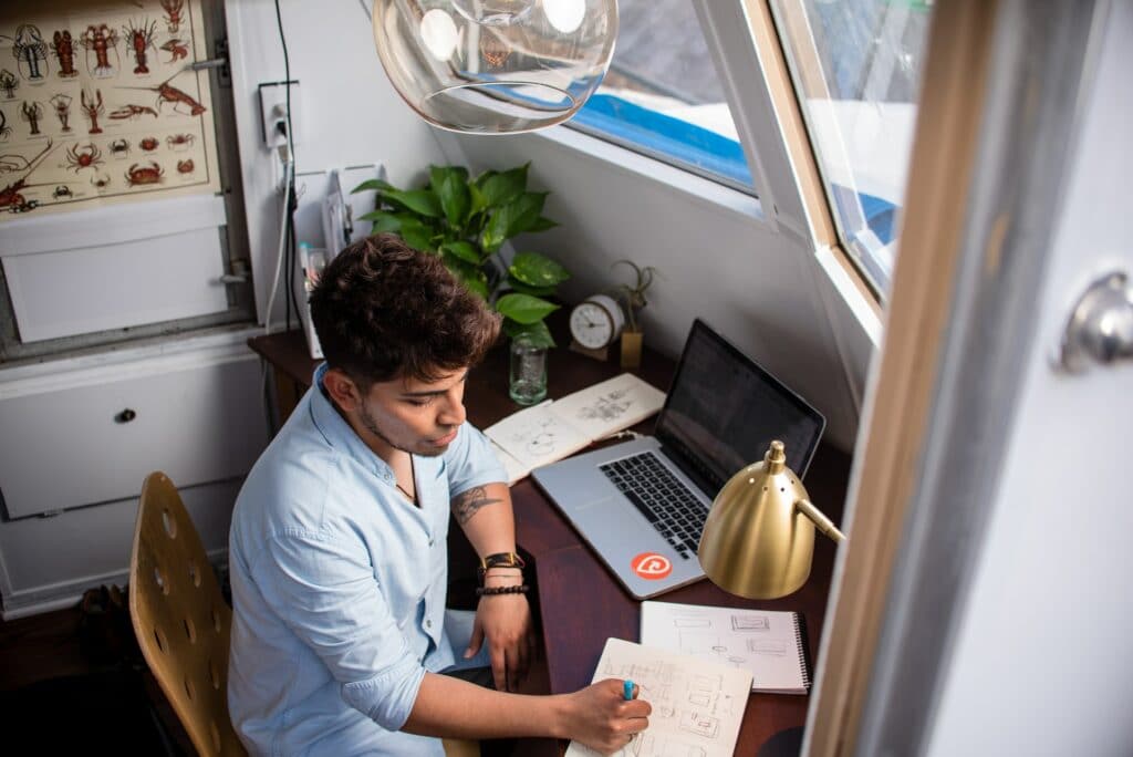 A person sits at their desk, in their own space, using their notebooks and laptop, one of the benefits of working from home.