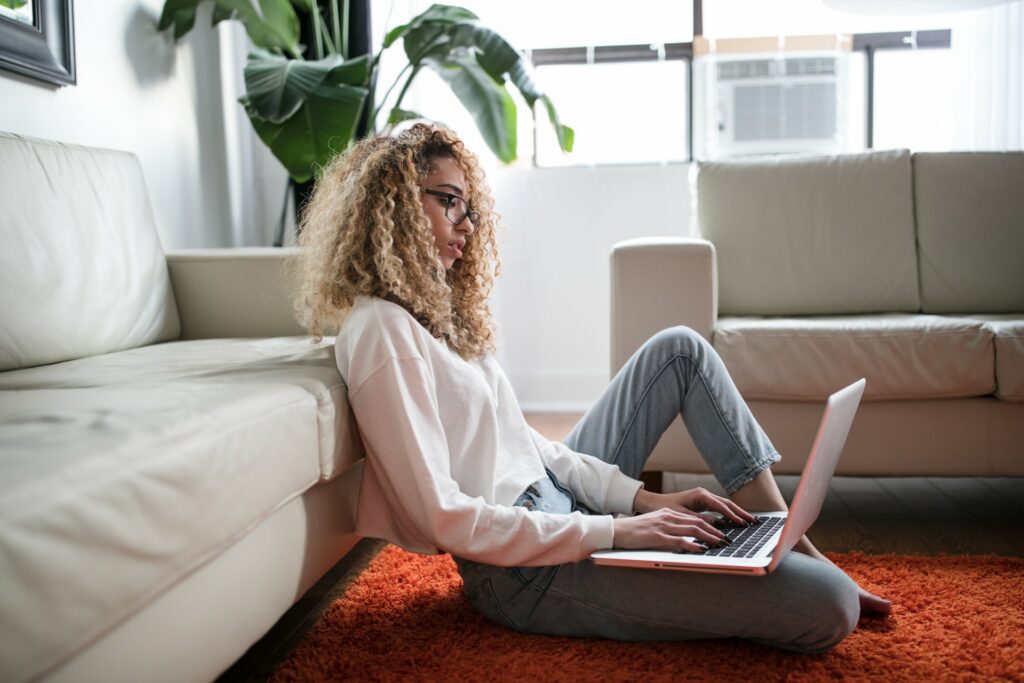 A person, sat on the floor using their laptop using some of the best work from home apps.