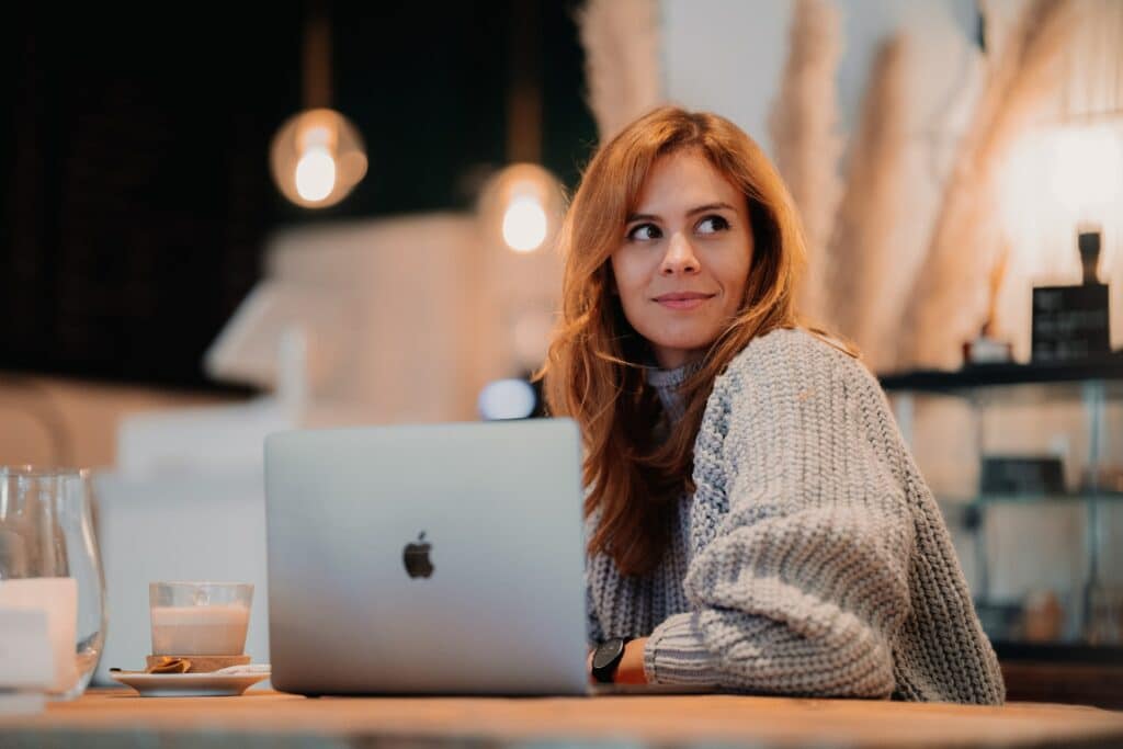 A person sat in a coffee shop using online tools for entrepreneurs on their laptop which is on the table in front of them along with a cup of coffee.