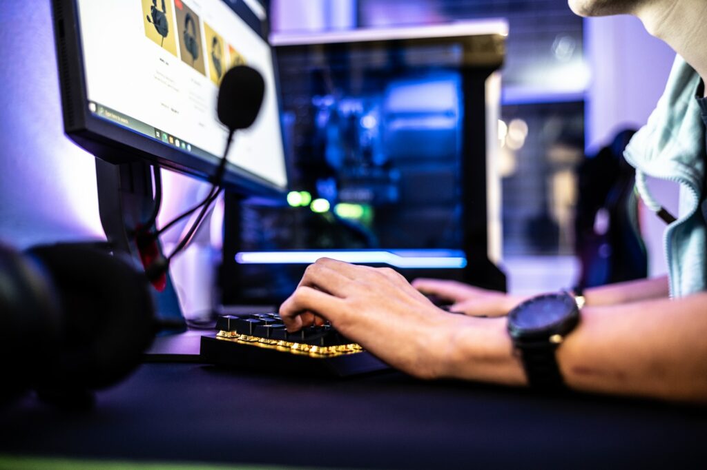 A streamer using a gaming keyboard with a large gaming PC in the background looking at gaming headsets to chase the next Twitch meta.