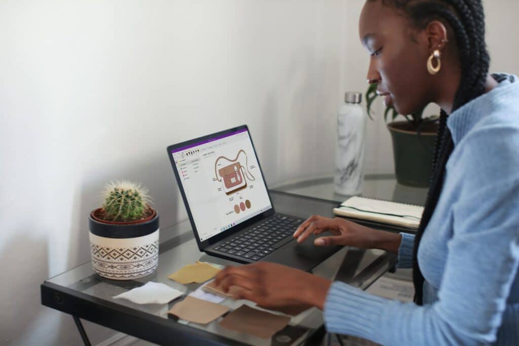 A person sat at a small desk at home using a laptop with a cactus on their desk deploying the best work from home routine.